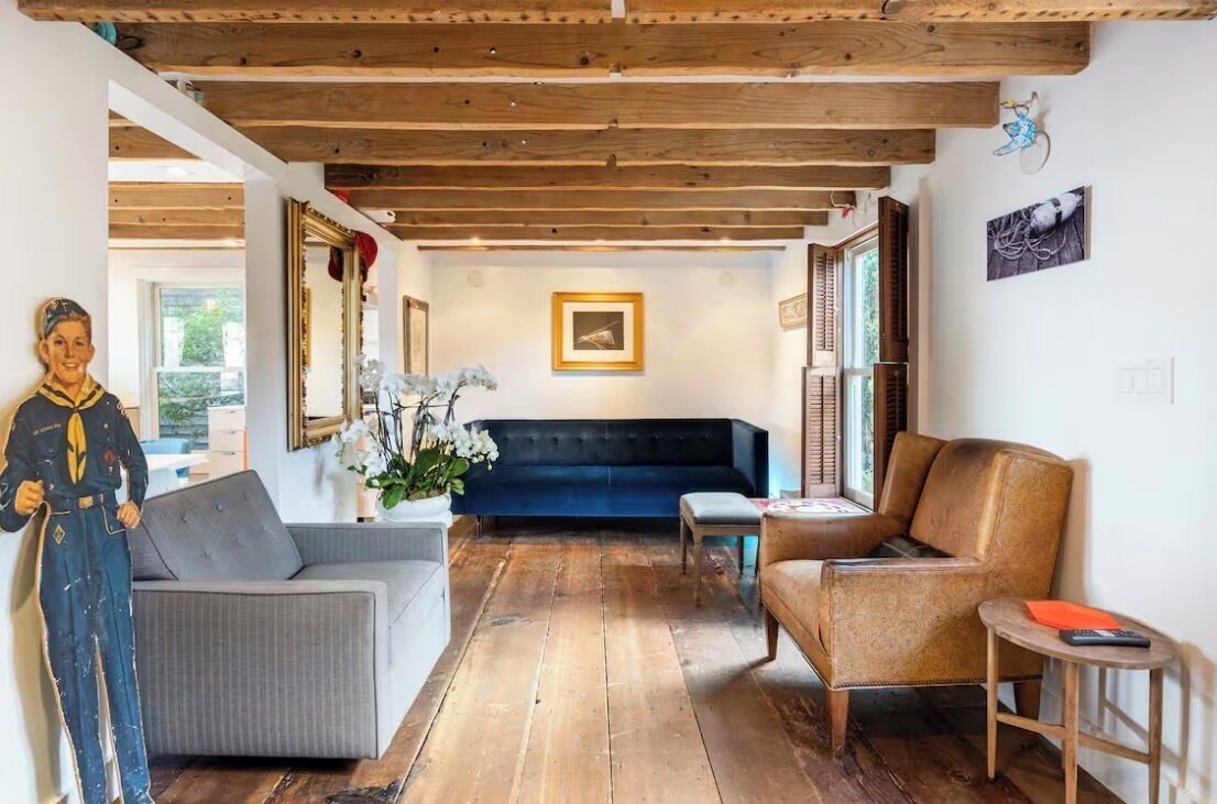 Ein Zimmer mit Holzboden, einem grauen Sofa, einem blauen Sofa, einem braunen Sessel und einem kleinen Tisch mit Fernbedienung.