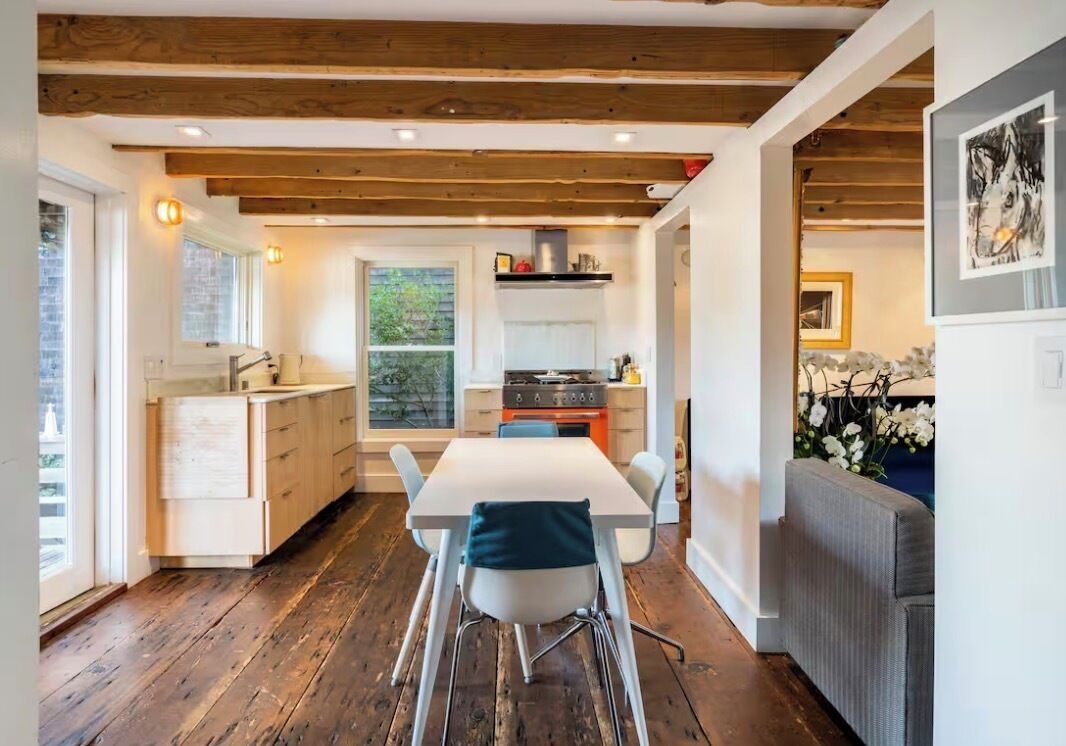 A modern kitchen with wooden beams, a dining area with a table and chairs, and a view of the outdoors.