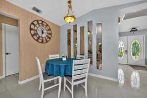 A dining area with a round table, white chairs, a blue tablecloth, a wall clock, and a chandelier. - Canal Paradise Pool, Kayaks, BBQ & Firepit (Port Charlotte)