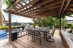 An outdoor deck with a pergola, a table with chairs, and a view of a marina. - Canal Paradise Pool, Kayaks, BBQ & Firepit (Port Charlotte)