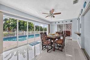 A spacious indoor area with a dining table, chairs, a ceiling fan, and a view of an outdoor swimming pool. - Canal Paradise Pool, Kayaks, BBQ & Firepit (Port Charlotte)