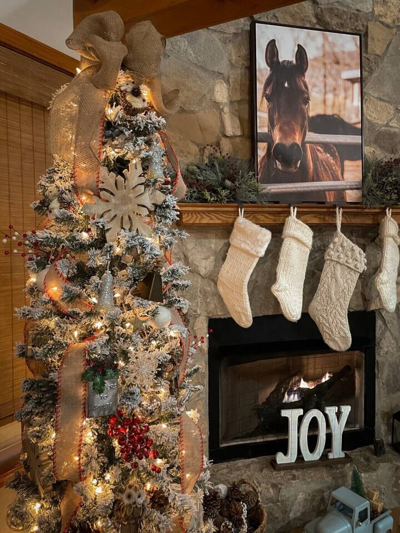 A decorated Christmas tree with lights and ornaments, a fireplace with stockings, and a framed picture of a horse.