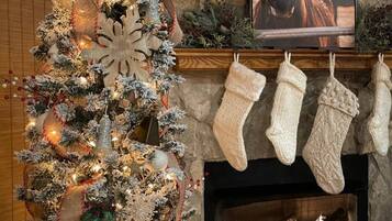 A decorated Christmas tree with lights and ornaments, a fireplace with stockings, and a framed picture of a horse.