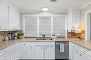 A kitchen with white cabinetry, a stainless steel sink, and a dishwasher. - Charming Historic District Home  Walking Distance to Kyle Field & TAMU Campus (College Station)