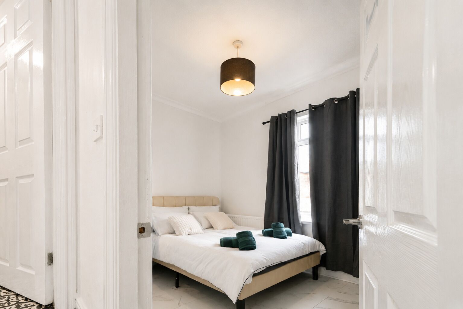 A bedroom with a bed, a hanging light fixture, a window with curtains, and a door.