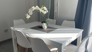 A modern dining area with a white table and chairs, a vase with white flowers, and a view of the outside through a window with a blue curtain. - Nature et ville - Duplex avec terrasse et jardin (Dammarie les lys)