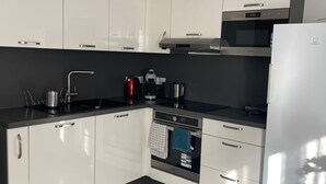 A modern kitchen with white cabinets, a black countertop, stainless steel appliances, and a tiled floor. - Nature et ville - Duplex avec terrasse et jardin (Dammarie les lys)