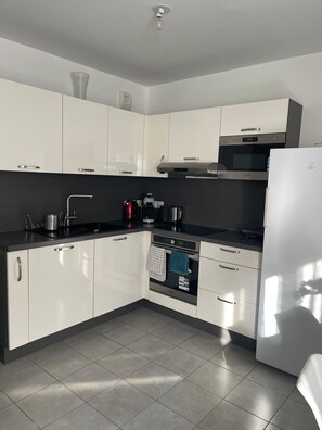A modern kitchen with white cabinets, a black countertop, stainless steel appliances, and a tiled floor. - Nature et ville - Duplex avec terrasse et jardin (Dammarie les lys)