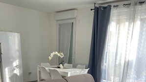 A modern living room with a sofa, a dining table with chairs, and a kitchen area with a refrigerator. - Nature et ville - Duplex avec terrasse et jardin (Dammarie les lys)