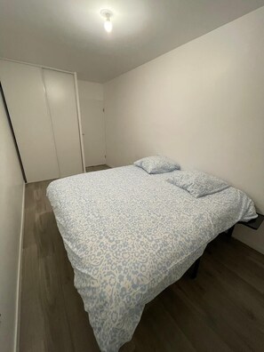 A single bed with a patterned bedspread and two pillows in a room with a wooden floor and white walls. - Nature et ville - Duplex avec terrasse et jardin (Dammarie les lys)