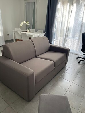 A modern living room with a sofa, a dining table with chairs, and a window with curtains. - Nature et ville - Duplex avec terrasse et jardin (Dammarie les lys)