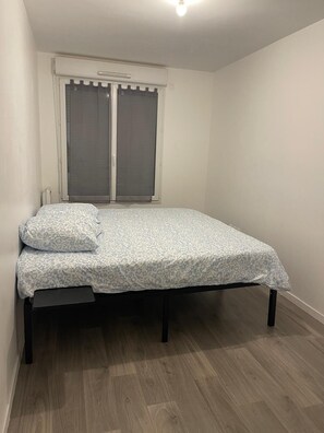 A single bed with a patterned bedspread and pillows, a window with blinds, and a light fixture on the ceiling. - Nature et ville - Duplex avec terrasse et jardin (Dammarie les lys)