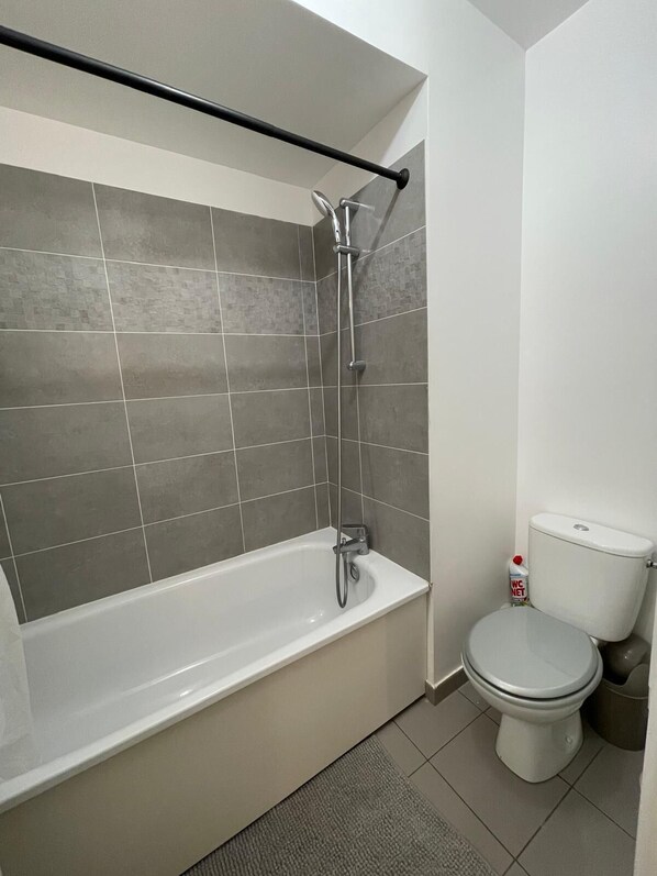 A bathroom with a bathtub, shower, toilet, and a handrail. - Nature et ville - Duplex avec terrasse et jardin (Dammarie les lys)