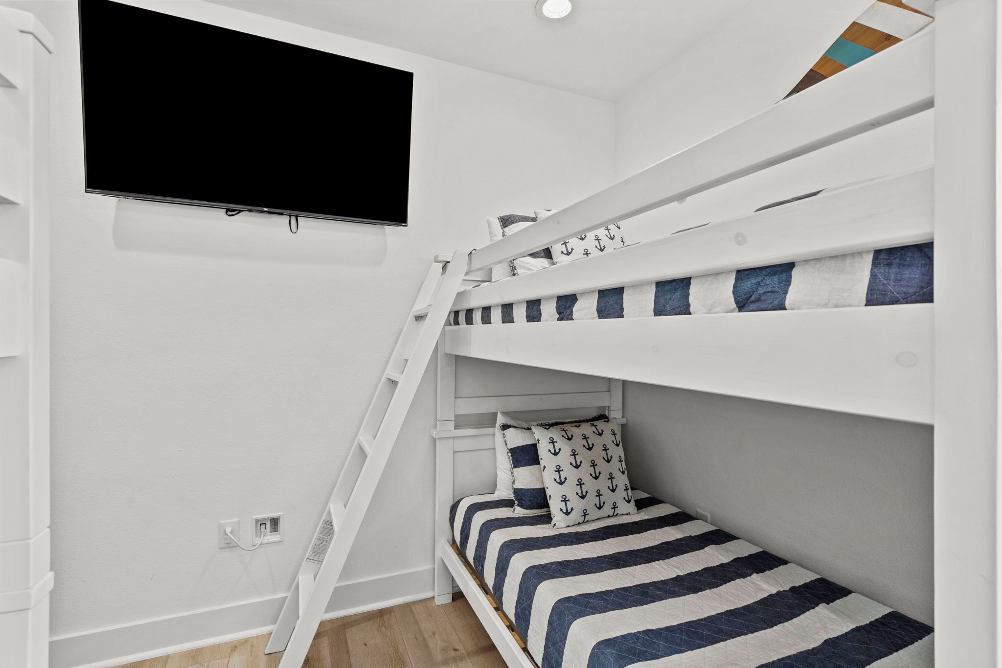 A bunk bed room with a TV mounted on the wall, a ladder, and a power outlet.