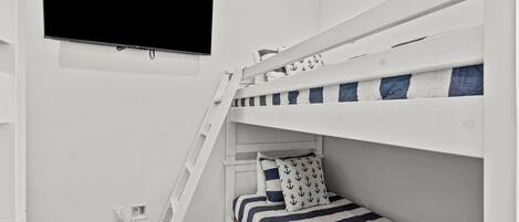 A bunk bed room with a TV mounted on the wall, a ladder, and a power outlet.