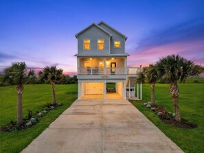 A two-story house with a front porch, a garage, and a well-maintained lawn. - 1-Min to Beach! New Home! Pets Welcome. 65 Inch Outdoor TV. King Bed! (Galveston)