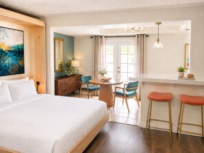 A hotel room with a large bed, a dining area with a round table, two bar stools, and a view of the outdoors. - The Villas Palm Springs (Palm Springs)