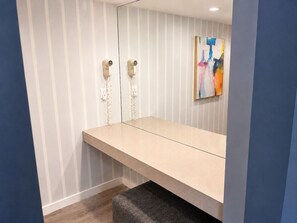 A bathroom with a bench, two hair dryers mounted on the wall, and a colorful abstract painting.
