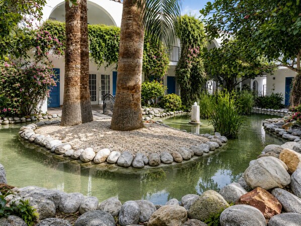 A courtyard with a central water feature, surrounded by rocks and palm trees.