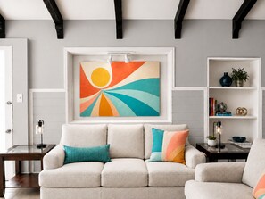 A living room with a sofa, a framed abstract painting, a side table, and a bookshelf.