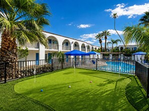 A pool area with a green lawn, a tennis court, and a building with arched windows.