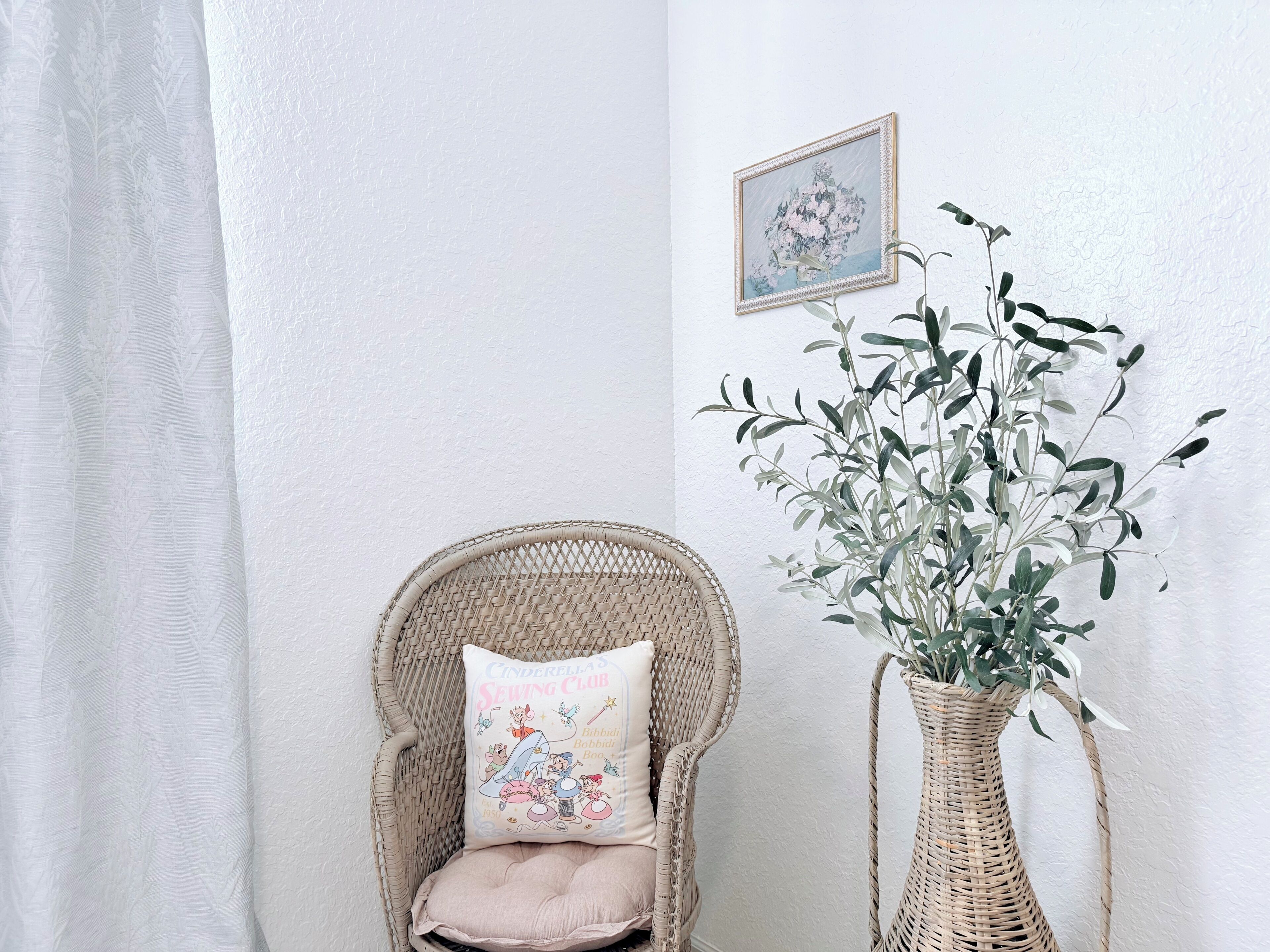 Une chaise en osier avec un coussin, un pot de fleurs en fibres tressées et un tableau encadré sur un mur blanc.