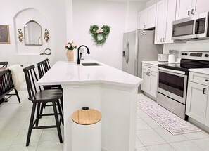 Une cuisine moderne avec des meubles blancs, un îlot central, un réfrigérateur, un four et un four à micro-ondes.