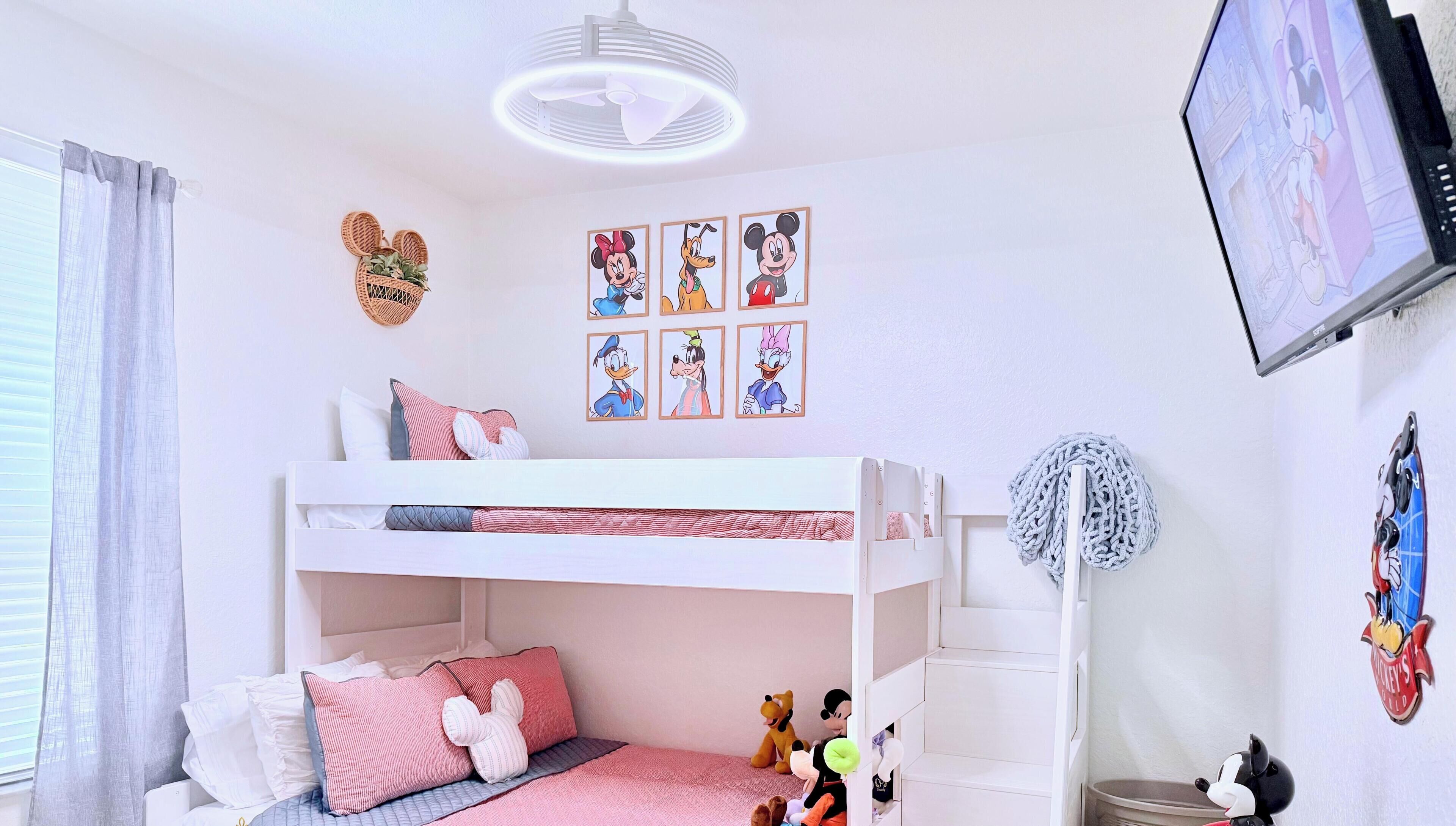 A child's bedroom with bunk beds, plush toys, wall art, and a television.