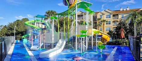 Ein Wasserpark mit mehreren Rutschen und Wasserspielen, umgeben von Gebäuden.