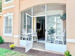 Une maison avec un porche couvert, des chaises blanches et une petite plante.