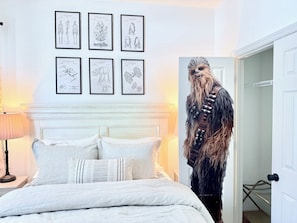 A bedroom with a bed, a nightstand, a lamp, and framed artwork on the wall. - *The Fairytale Condo*  2 Miles to Disney (Kissimmee)