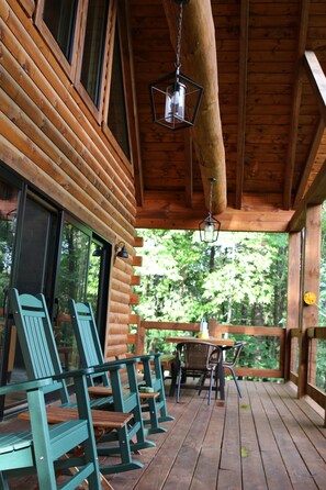 Eine Holzhütte mit Veranda, grünen Adirondack-Stühlen und einer hängenden Laterne.