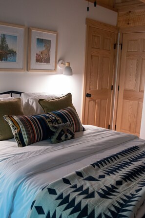 Ein Bett mit einem gemusterten Bettbezug und Kissen, eine Wandlampe und eine Tür mit Holzoptik.