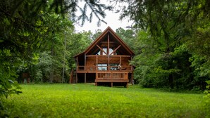 A wooden cabin with a balcony, surrounded by lush greenery. - Howdybrook Basecamp | Hocking Hills Cabin (Laurelville)