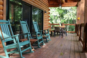 Eine Holzterrasse mit Schaukelstühlen und einem Tisch, mit Blick auf eine bewaldete Gegend.