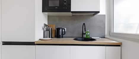 A compact kitchen with a microwave, kettle, and sink.
