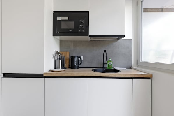 A compact kitchen with a microwave, kettle, and sink.