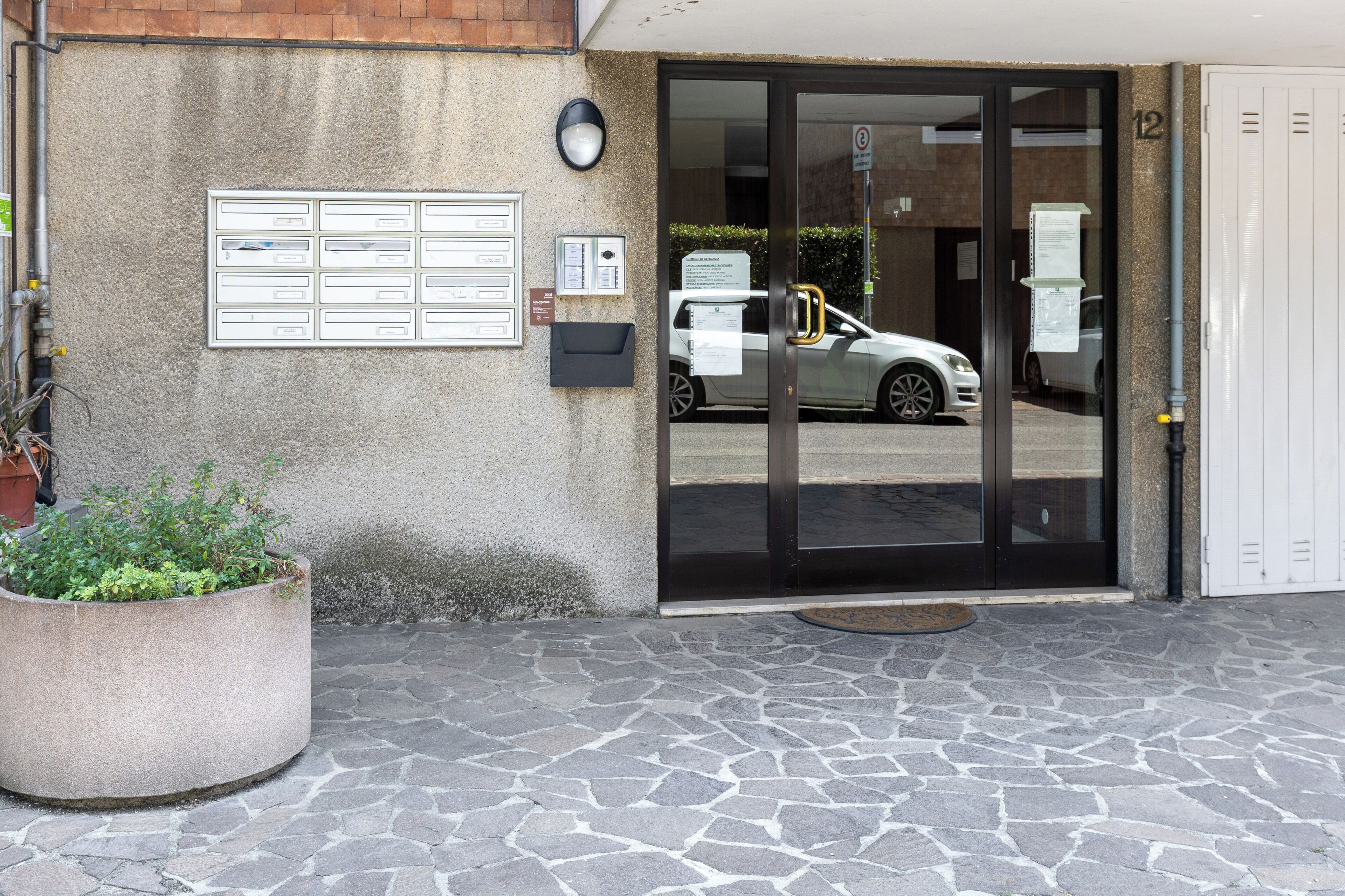 A building entrance with a glass door, a mailbox, and a car parked inside.