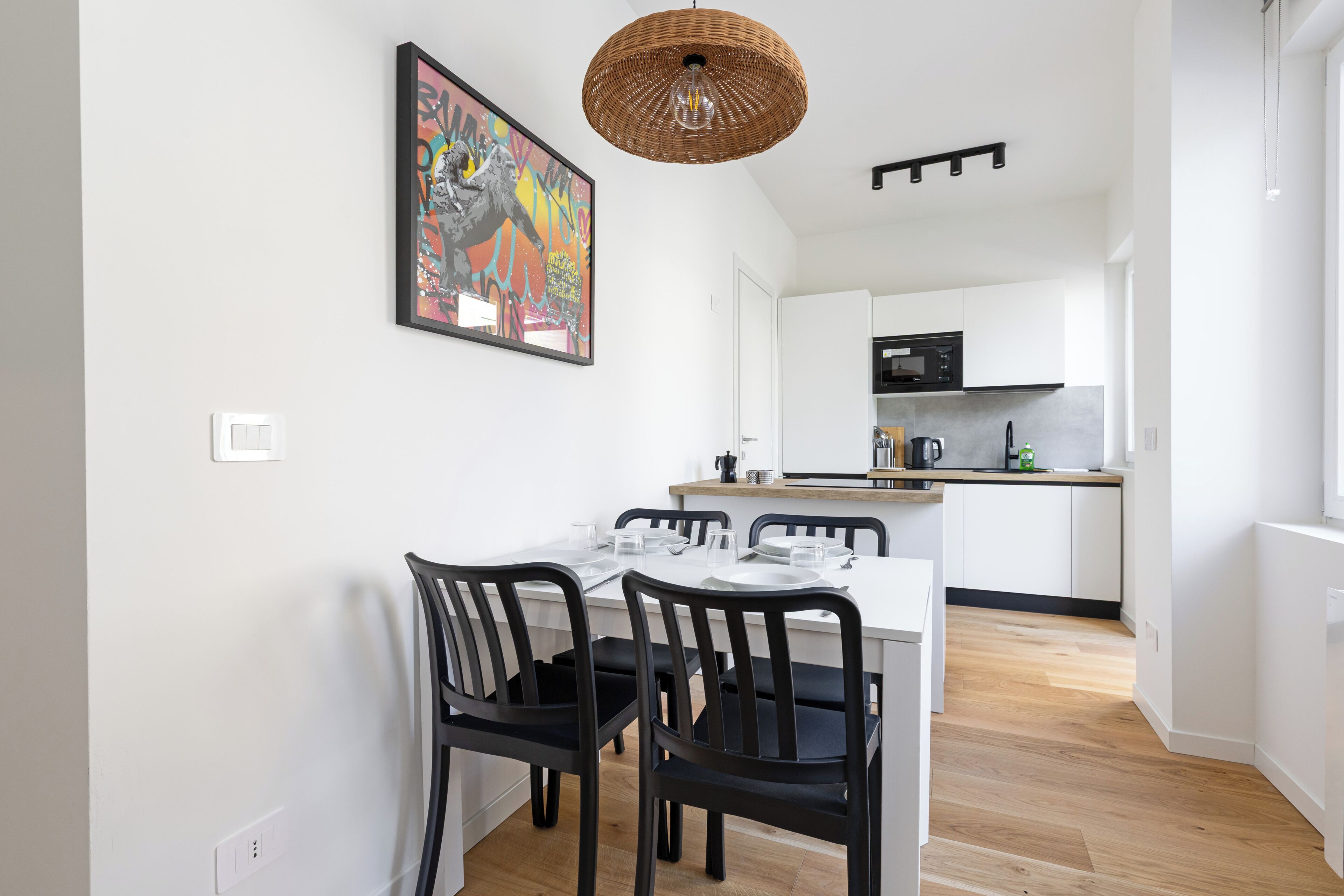 A modern kitchen with white cabinets, a black microwave, and a dining area with a white table and black chairs.