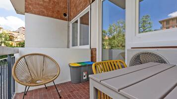 A balcony with a wicker chair, a trash bin, and a table.