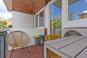 A balcony with a wicker chair, a trash bin, and a table.