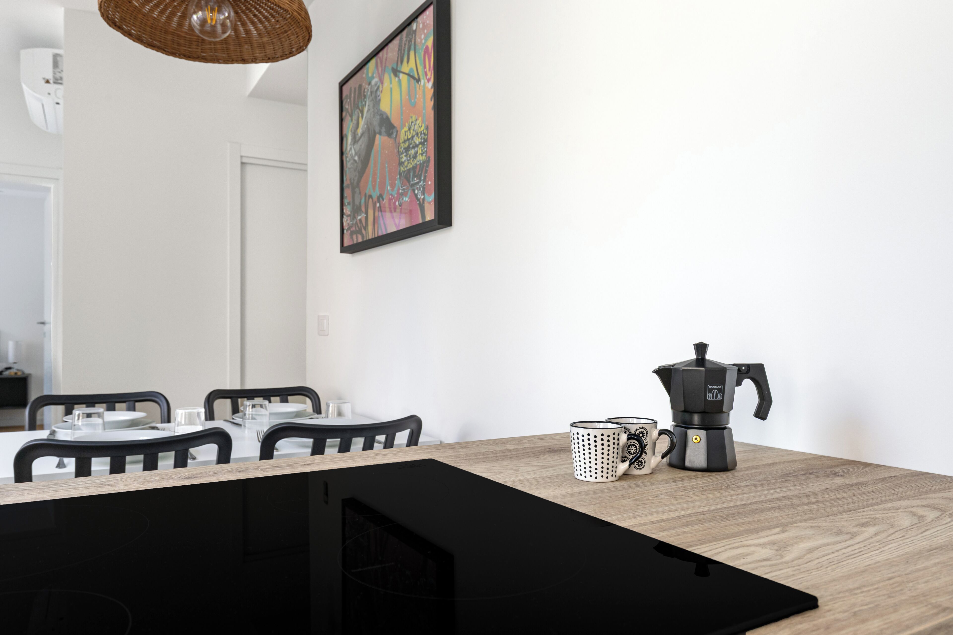 A dining area with a table set for four, a coffee maker, and a framed artwork on the wall.
