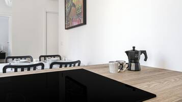 A dining area with a table set for four, a coffee maker, and a framed artwork on the wall.