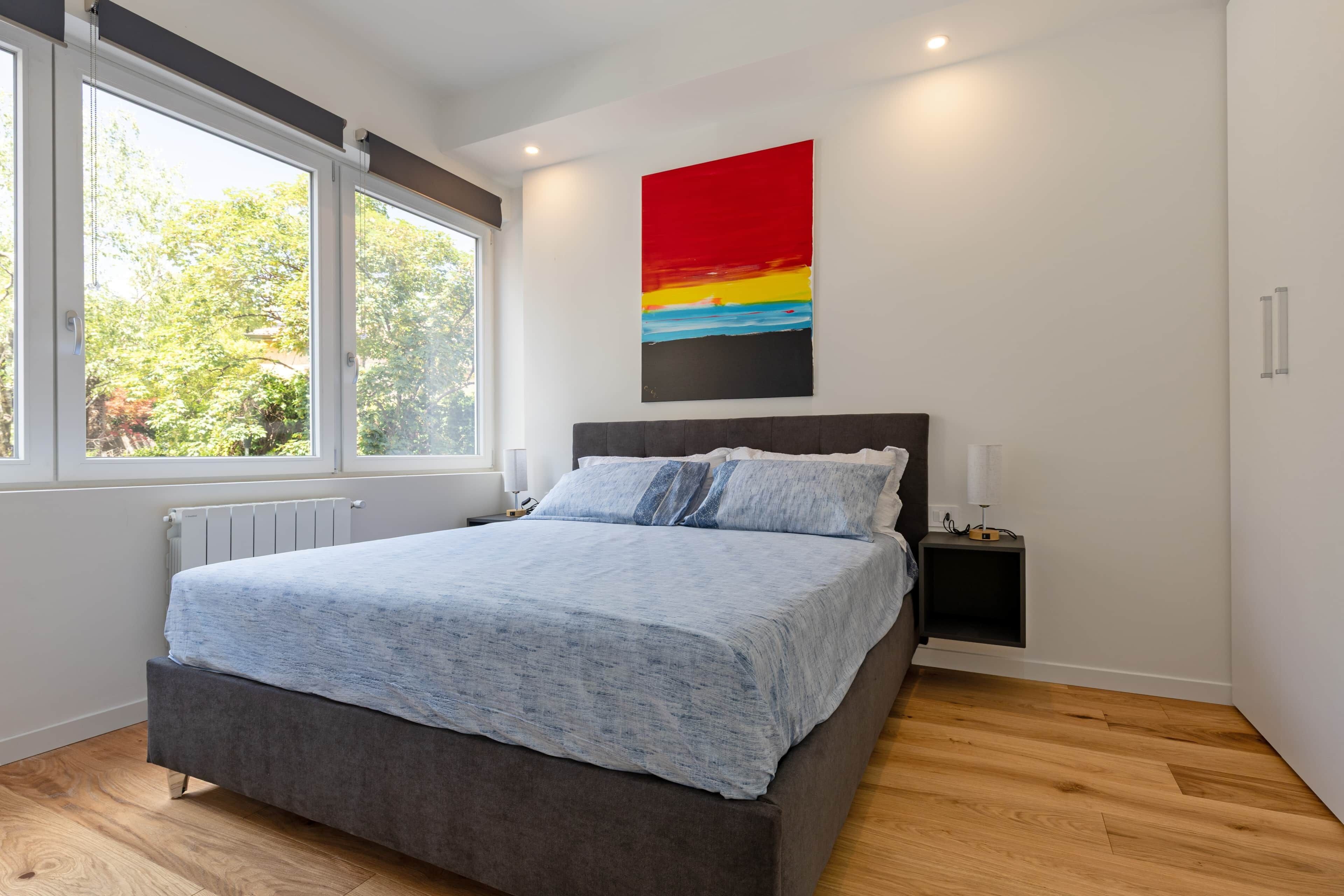 A bedroom with a bed, a nightstand, a radiator, and a window.