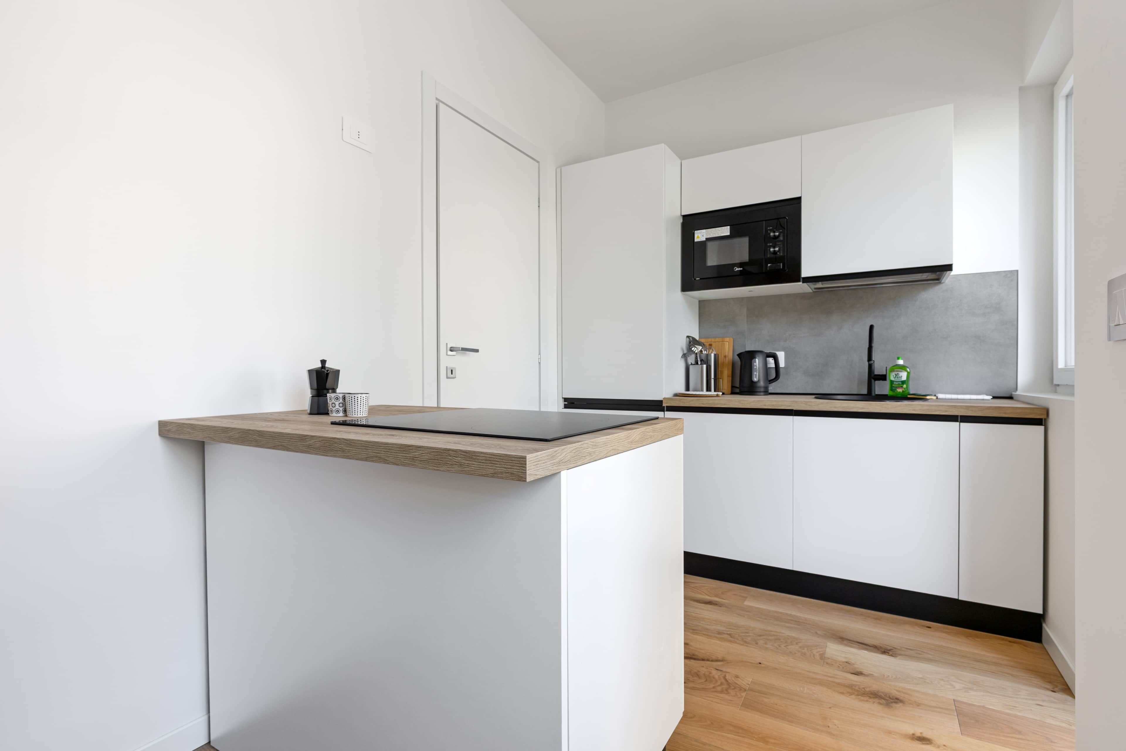 A modern kitchen with white cabinets, a black microwave, and a wooden countertop.