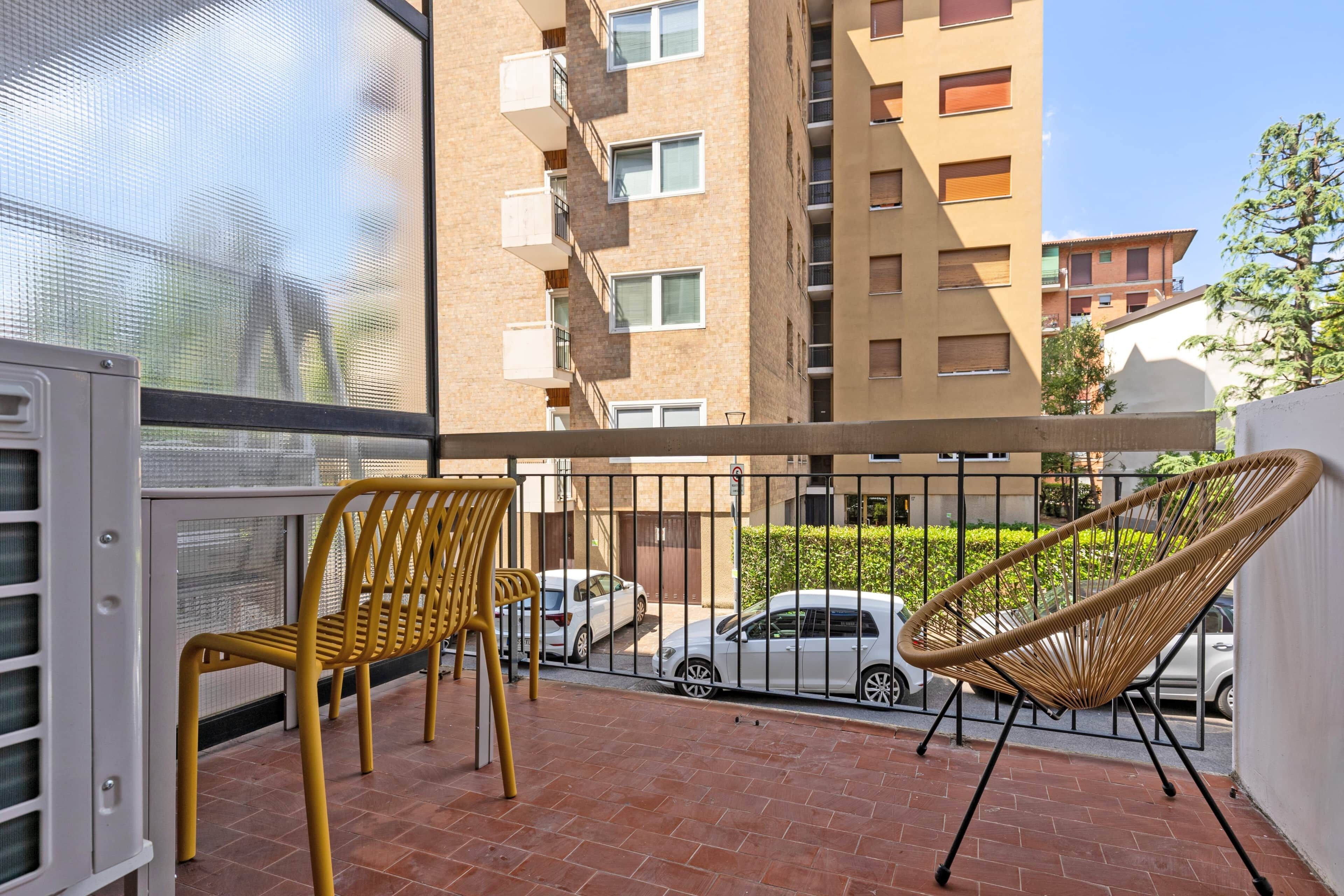 A balcony with two chairs, a white car parked in the background, and a building with multiple windows and balconies.