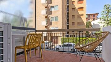 A balcony with two chairs, a white car parked in the background, and a building with multiple windows and balconies.