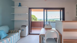 Ein modernes Zimmer mit einer Couch, einem Tisch und einem Stuhl. Ein Balkon bietet Blick auf das Meer.