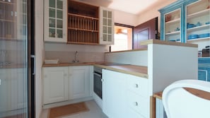 Una cucina compatta con mobili bianchi, forno integrato e piano di lavoro in legno.