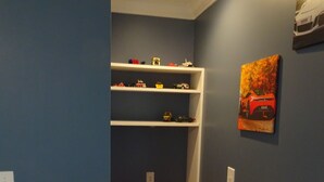 A hallway with blue walls, white trim, and a wooden bench. There are shelves with toys and a painting of a car on the wall.